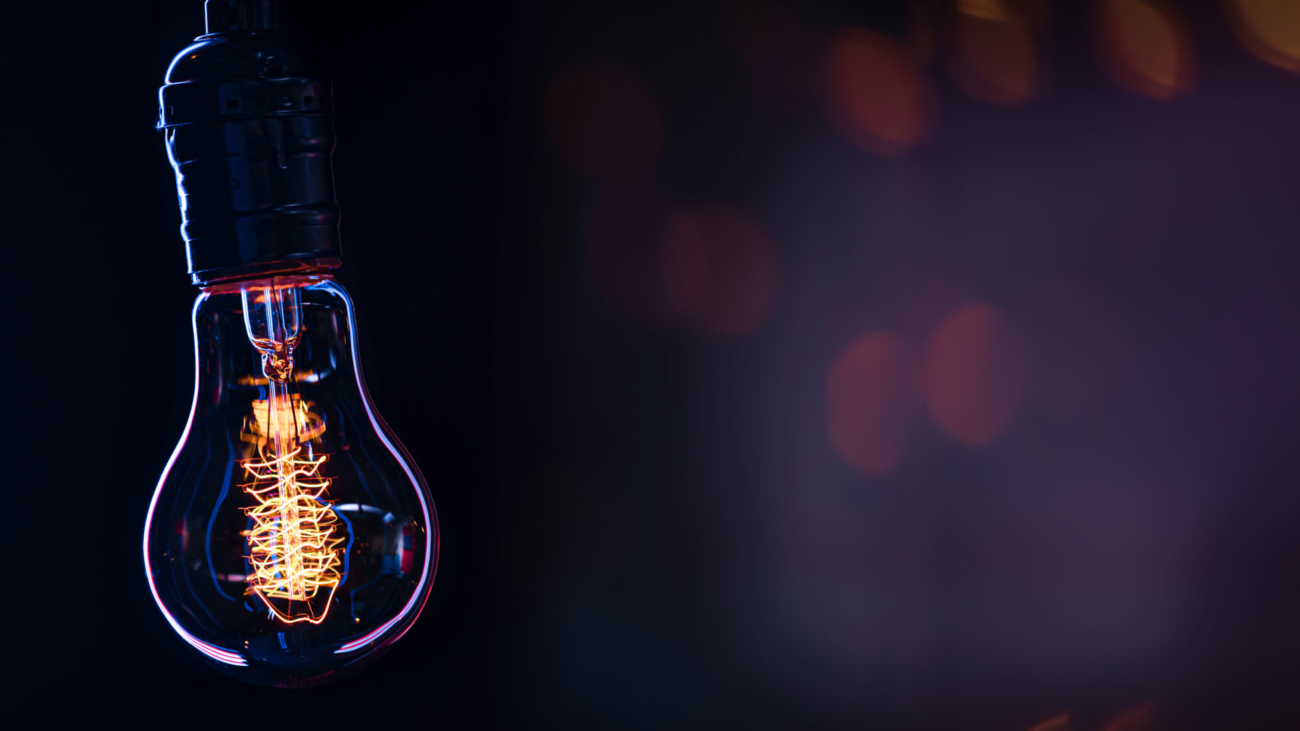 A burning lamp hangs in the dark on a blurred background. Space for text. High quality photo. A light bulb glows in the dark.
